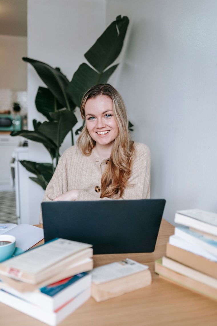 Woman smiling while using her laptop near a stack of books